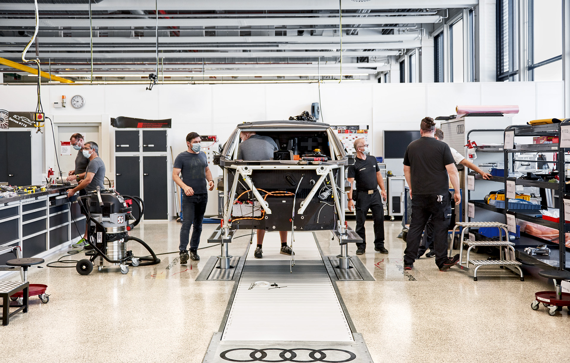 Audi Sport employees work on the rally car’s elevated cage in a workshop. 