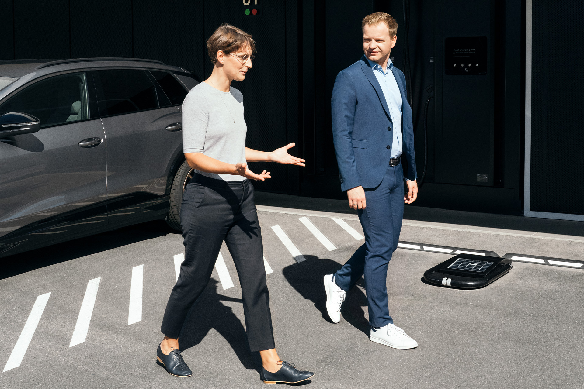Sustainability experts Dr Johanna Klewitz and Malte Vömel walk across the parking lot in front of the Audi charging hub in Nuremberg.