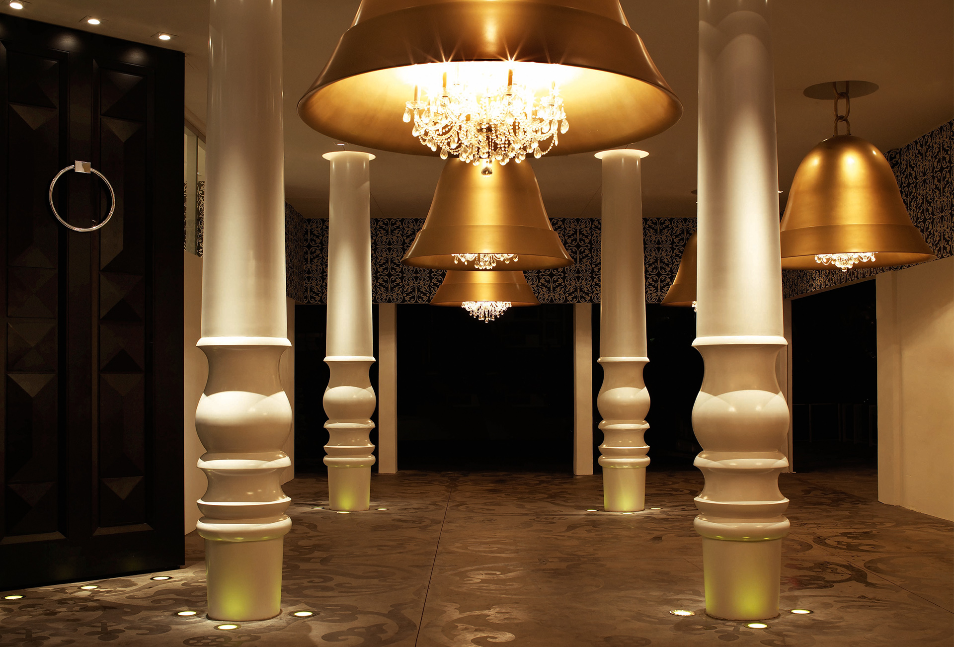 Huge, golden bell-lamps hang in a hall between white columns.